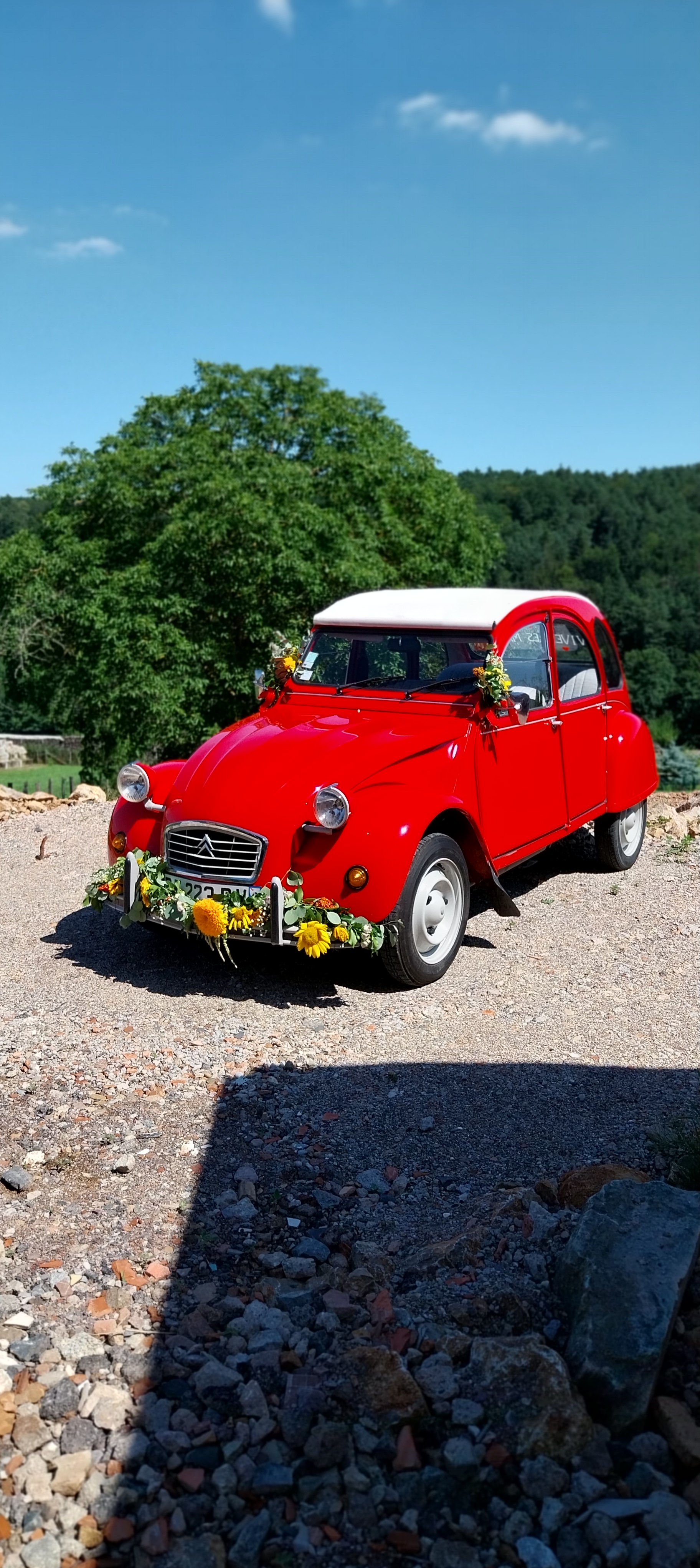 Citroën 2 chevaux rouge décapotable, décorée de fleurs dans les tons jaunes orangés.